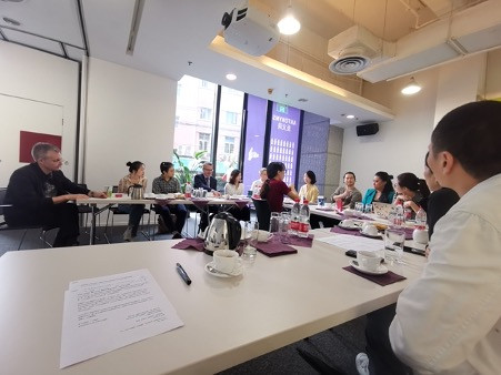 14 people are sitting around a table, having a discussion